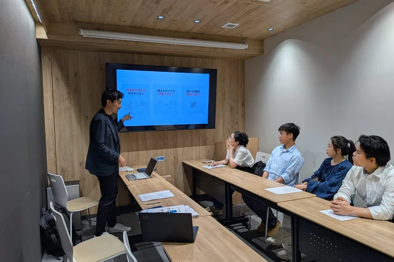 会議室のモニターに学習の課題を示したスライドを映し、講師が外国人材4名に説明している様子